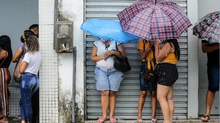 Pessoas com guarda-chuvas se abrigando próximo de comércios
