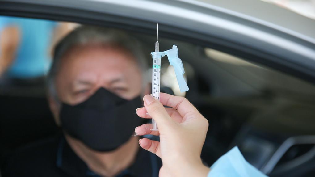 uma mão segurando uma agulha com vacina contra a Covid-19 na frente de idoso
