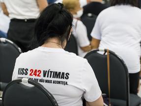 Pessoa usa blusa branca com escritos nas costas que diz Kiss 242 vítimas