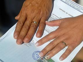 Mãos com alianças sobre certidão de casamento