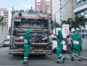 caminhão de lixo recolhendo material em frente a condomínio