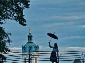 Uma mulher ergue um guarda-chuva com um dos braços enquanto anda em cima de uma ponte