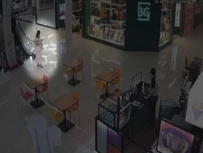 Imagem de câmera de segurança mostra Anic caminhando olhando o celular em um shopping