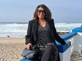 Maria Solange sentada em parapeito em praia. Ela é uma mulher negra e de cabelos cacheados