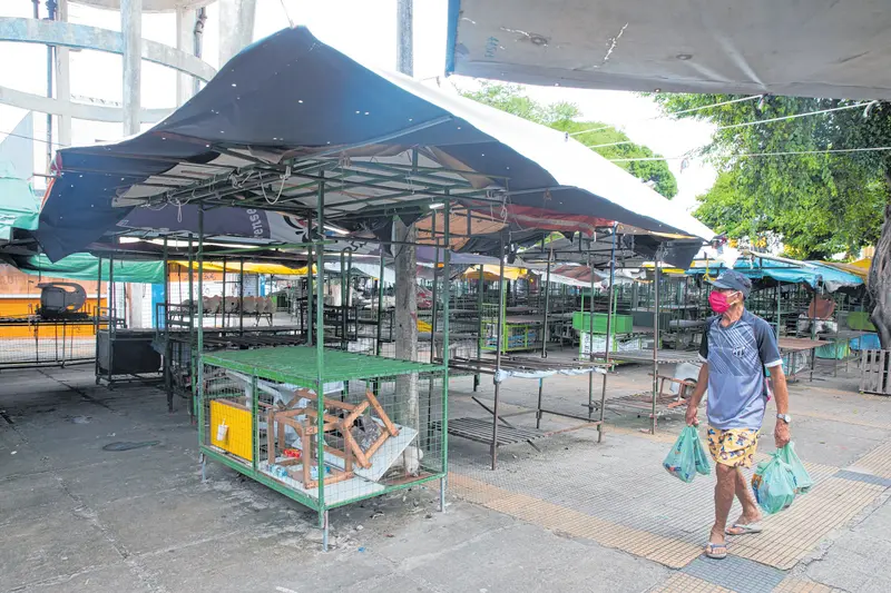 Homem carrega sacolas em frente a barracas de feira vazias