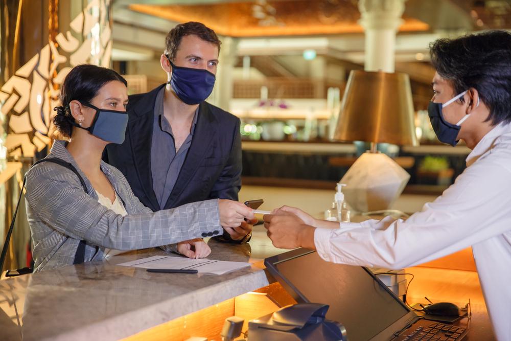 Imagem de turistas usando máscaras na recepção de um hotel.