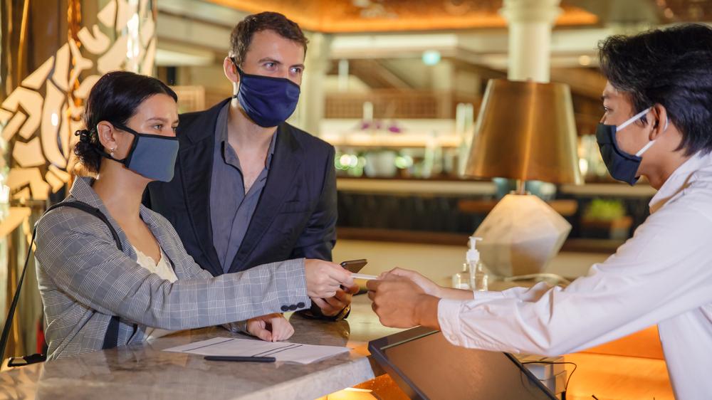 Imagem de turistas usando máscaras na recepção de um hotel.
