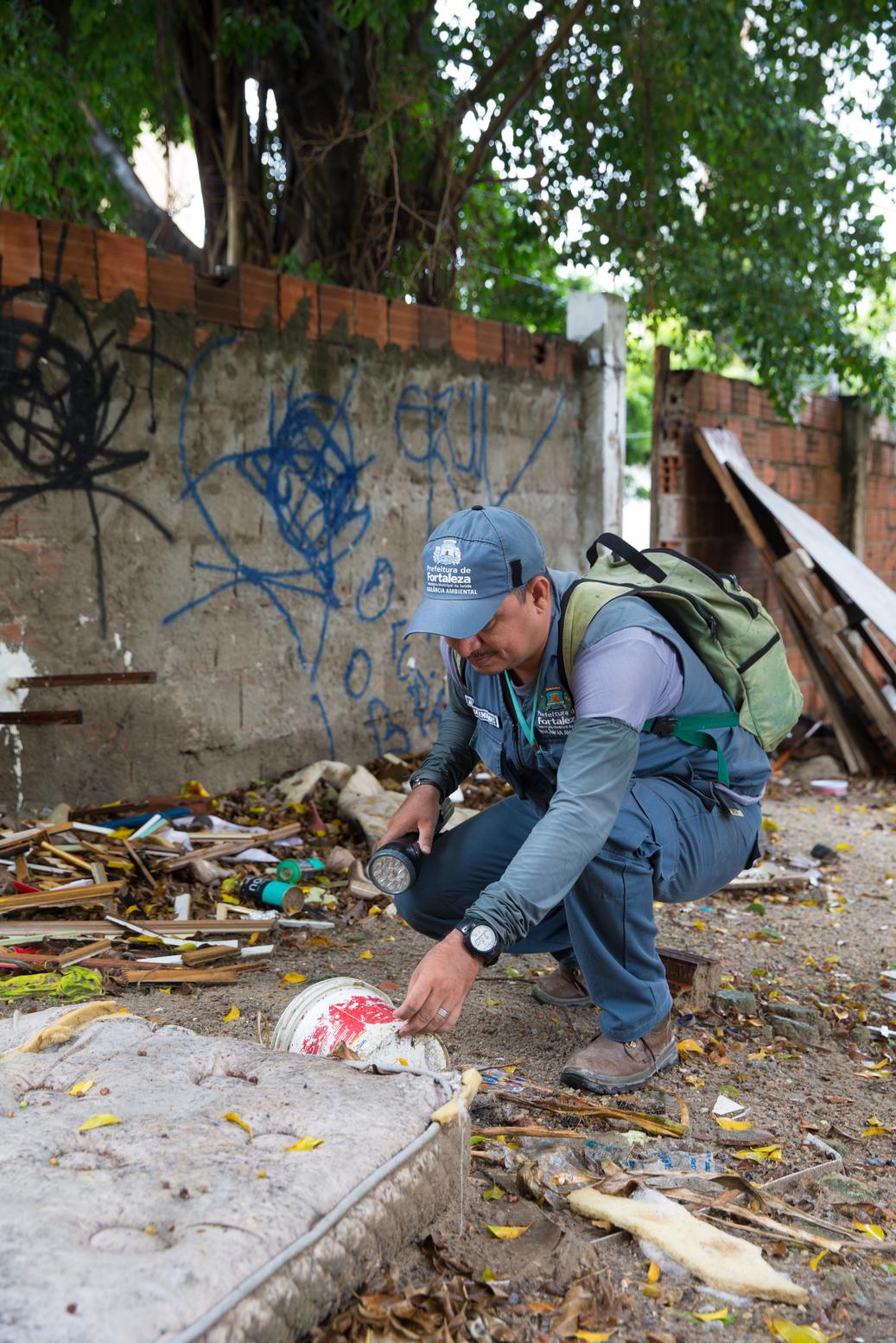 Na imagem, o agende de endemia procura por focos de aedes aegypti em um terreno.