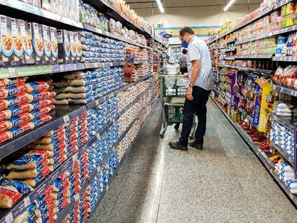 Homem confere preços em prateleiras de supermercado