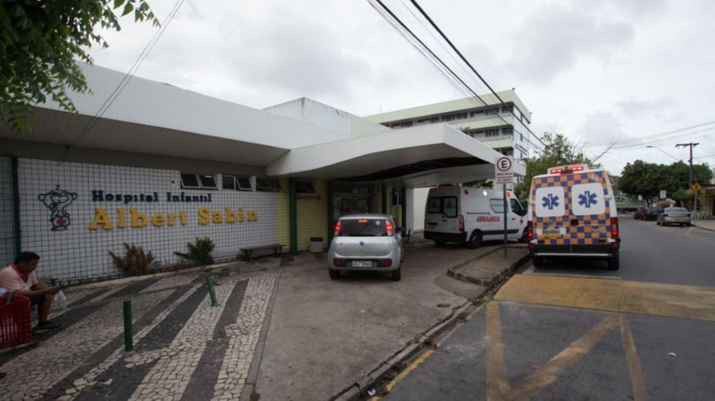 Fachada do hospital infantil Albert Sabin. Em frente à entrada há um carro cinza e duas ambulâncias.
