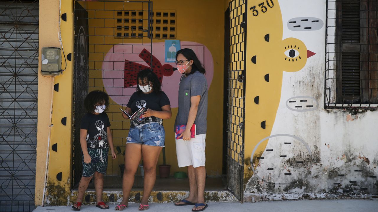 Estes são João Gabriel, de 7 anos, a mãe Paula Amanda, de 31 anos, e o amigo William Soares, de 19 anos, de máscara, segurando livros em frente a uma biblioteca comunitária no Curió