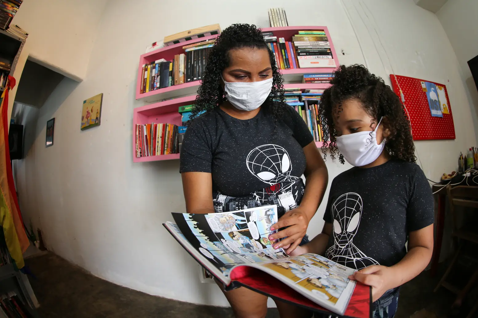 Esta é uma imagem da mãe Paula Amanda com o filho João Gabriel, ambos de máscara, folheando um livro