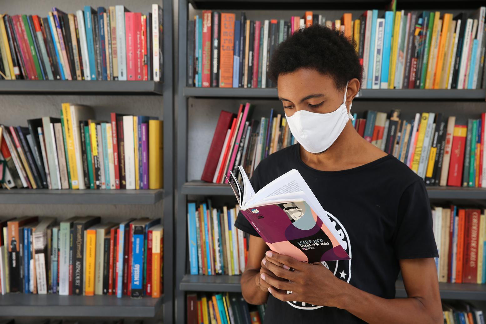 Este é um rapaz jovem, de máscara, lendo um livro na Biblioteca Viva, do Barroso