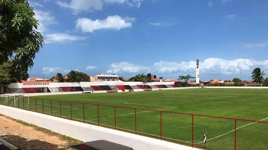 Estádio do Ferroviário Atlético Clube com arquibancadas em cores vermelha, preta e branca, cercado por árvores e céu nublado, celebrando o sucesso do esporte e do clube.