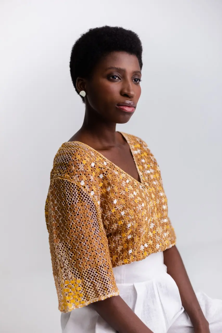 Esta é uma modelo negra com uma blusa de manga amarela toda feita em renda de bilro