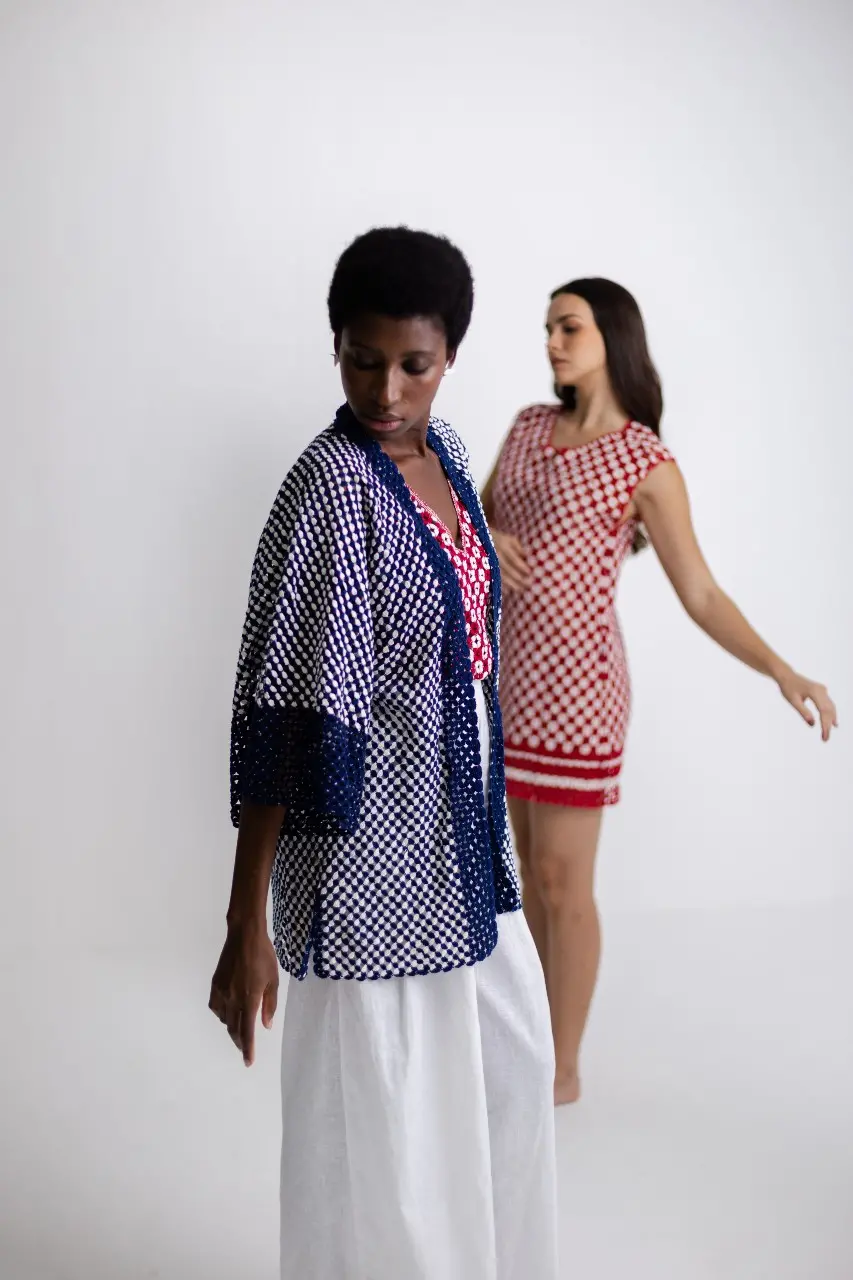 Esta é a foto de um ensaio da coleção Olê Rendeiras. Uma modelo está usando um kimono azul e a outra um vestido vermelho em renda de bilros