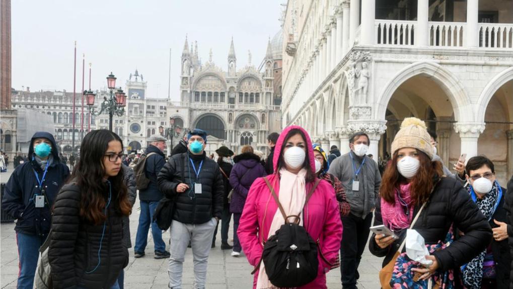 Grupo de turistas de máscara em frente a ponto turístico em Veneza