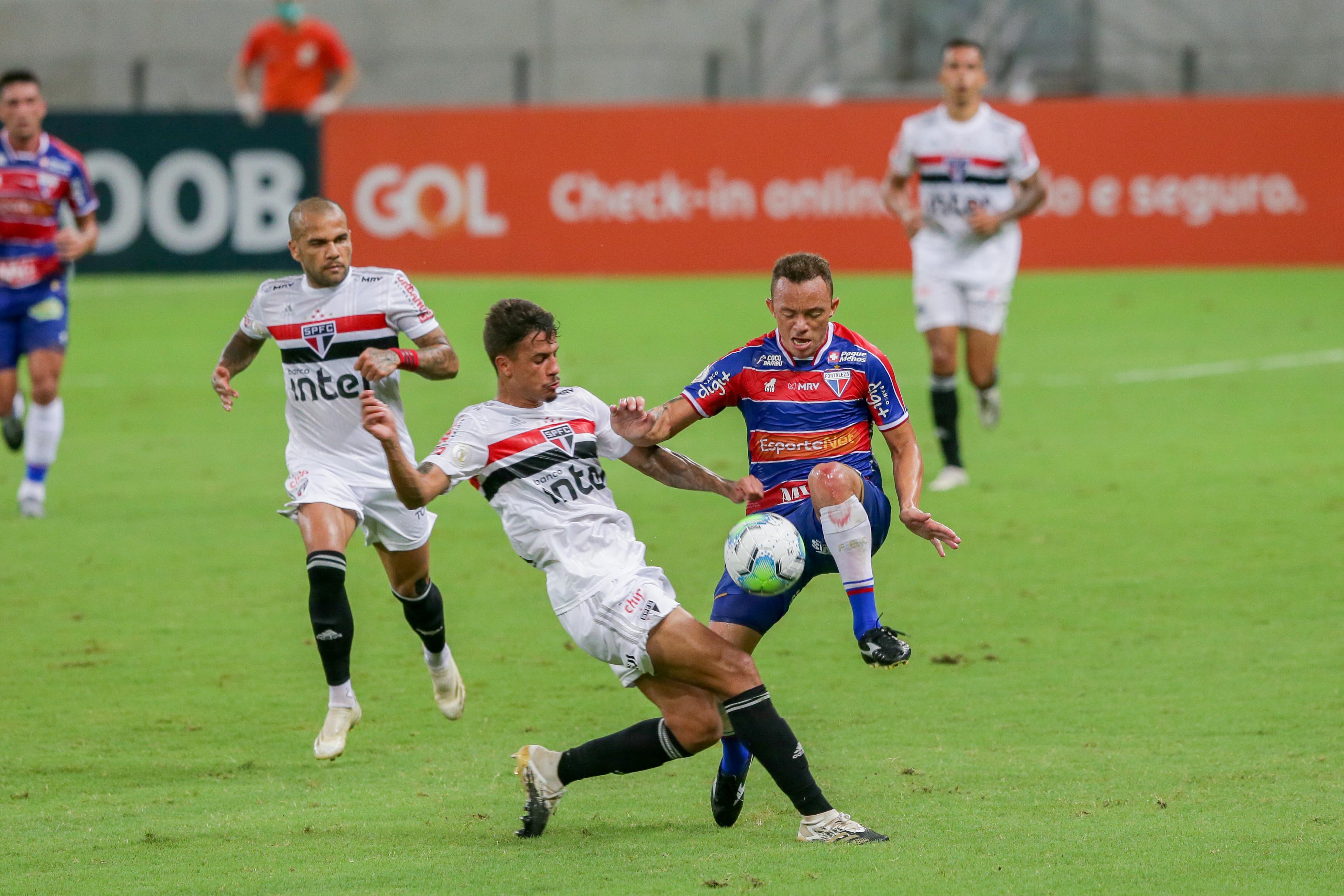 Carlinhos, do Fortaleza, pulando e dividindo bola com jogador do São Paulo, sendo observado por Daniel Alves