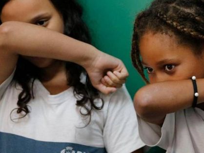 Crianças com farda escolar tapando o nariz com o braço