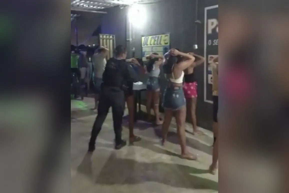 Várias pessoas, a maioria mulheres, de costas, com as mãos na cabeça e as pernas entreabertas, sendo revistadas por uma policial