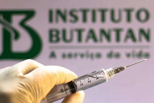 Está é uma imagem de uma seringa com a logo do Instituto Butantan como plano de fundo.