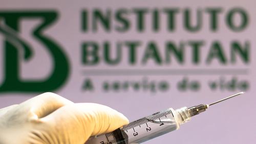 Está é uma imagem de uma seringa com a logo do Instituto Butantan como plano de fundo.