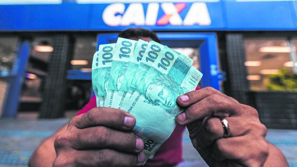 Homem segurando notas de 100 reais retirados do auxílio emergencial