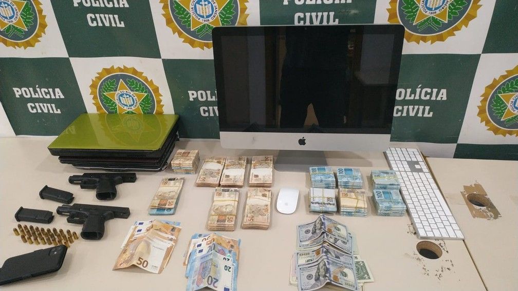 Armas, munição, dinheiro e computador dispostos em uma mesa da polícia civil do Rio de Janeiro