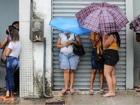 Pessoas com guarda-chuvas se abrigando próximo de comércios