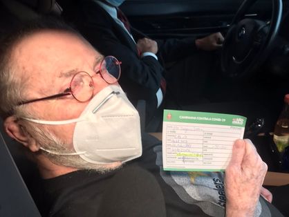 Jô Soares dentro do carro apresentando o seu cartão de vacinação.