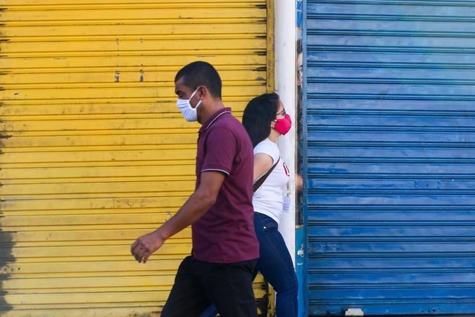 Pessoas com máscaras passam em frente a lojas fechadas