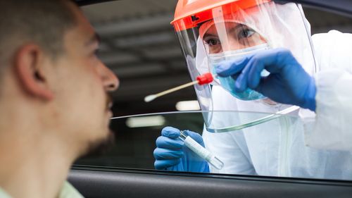 Trabalhador médico do Reino Unido realizando verificação de drive-thru COVID-19, colhendo amostra de espécime de esfregaço nasal de paciente masculino através da janela do carro, diagnóstico de PCR para presença de Coronavírus