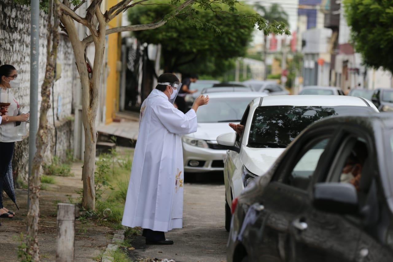 Padre entregando hóstia a católicos que esperam em uma fila de carros
