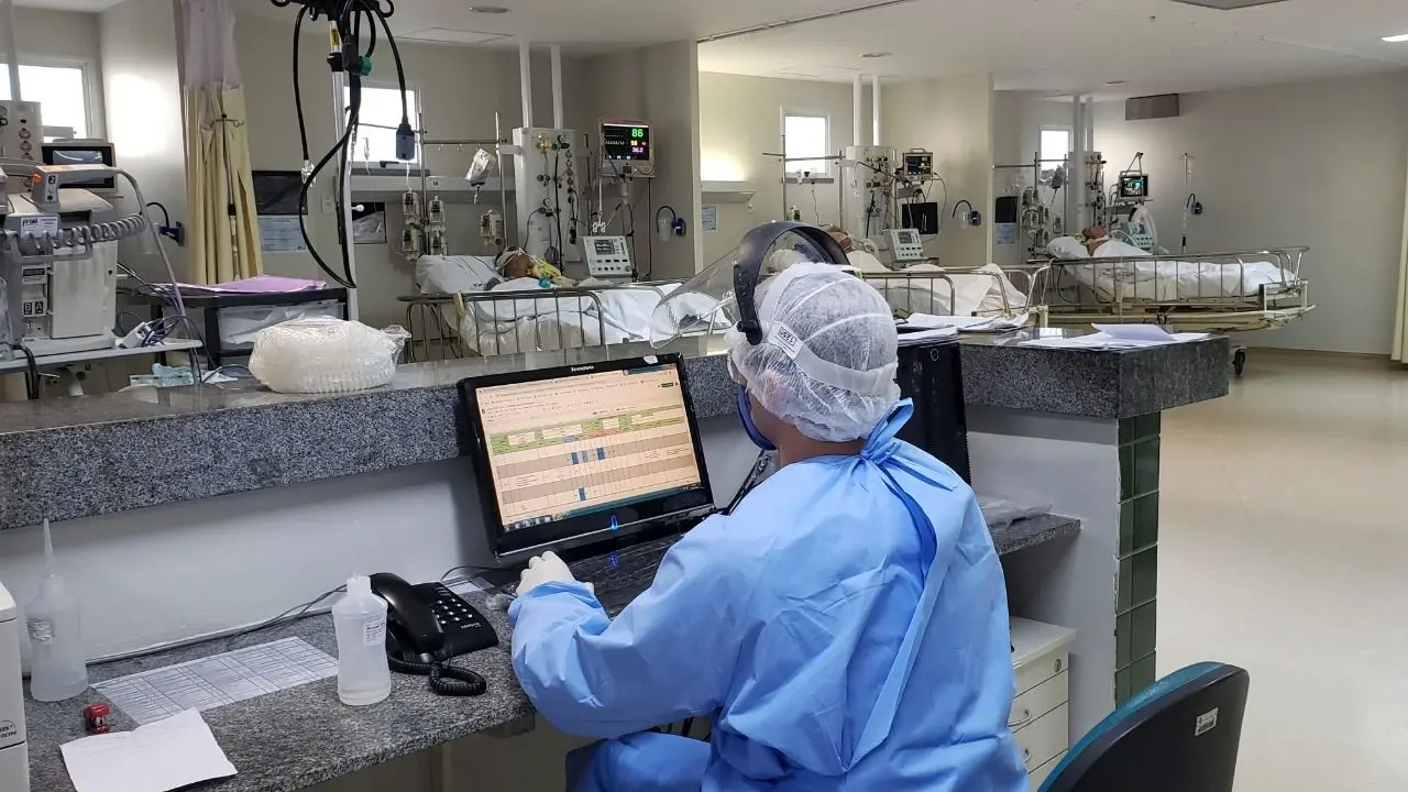 Pacientes internados em leitos de UTI e profissional da saúde acessando dados em computador