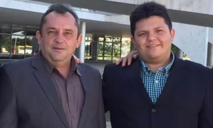 Do lado esquerdo da imagem, o ex-prefeito de Bela Cruz, Carlos Antônio, de paletó. Ao lado dele, o atual prefeito da cidade, Netim Moraes, também de paletó. Eles estão abraçados e posando para a foto