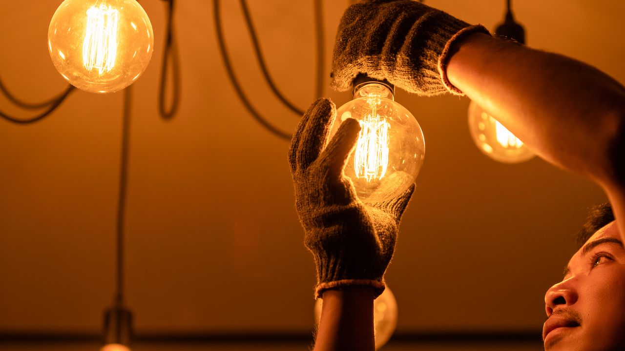 Homem troca iluminação de lâmpadas de energia elétrica