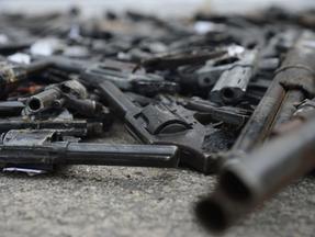 Armas de fogo de diversos tipos, entre pistolas, revólveres e espingardas jogadas no chão