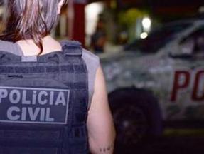 Policial civil feminina de costas usando colete à prova de balas e perto de viatura