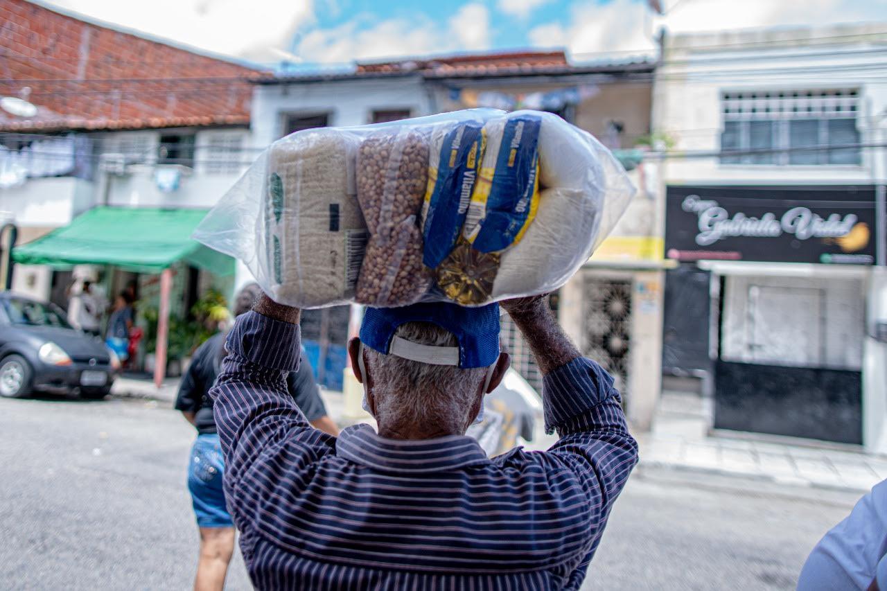 Idoso carregando cesta básica na cabeça