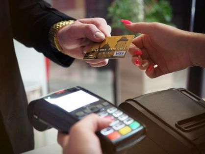 Duas mãos segurando cartão de crédito e uma máquina de pagamento