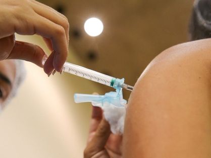 Profissional da saúde aplicando vacina contra a Covid-19 no braço esquerdo de uma mulher