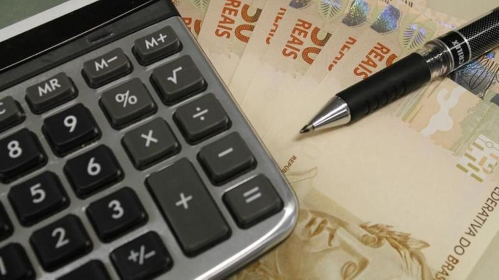 Calculadora, cédulas de cinquenta reais e uma caneta representando a negociação de dívidas