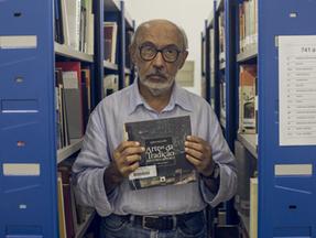 Gilmar de Carvalho segurando livro entre estantes