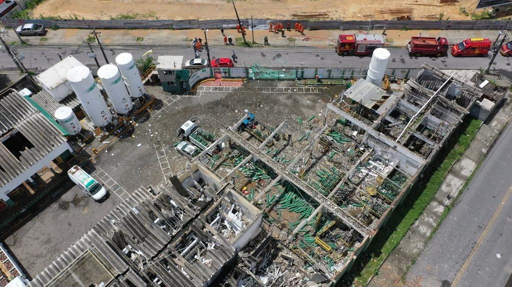 Vista aérea da destruição da fábrica da White Martins após a explosão, com cilindros de oxigênio verdes espalhados pelo chão, vidros e telhados quebrados