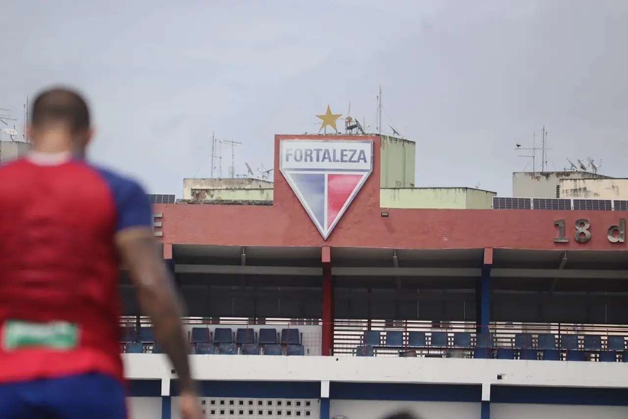 Escudo do Fortaleza no fundo com atleta desfocado na frente