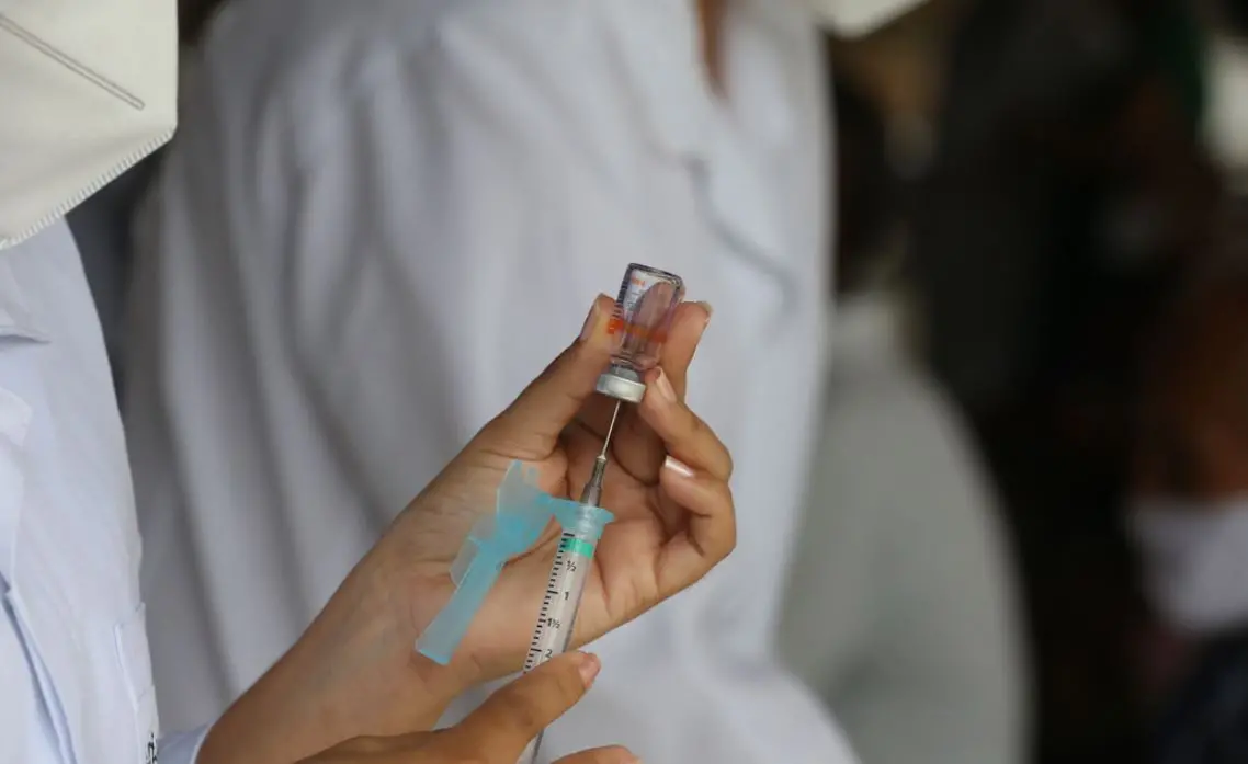 Enfermeira segurando dose de CoronaVac e seringa