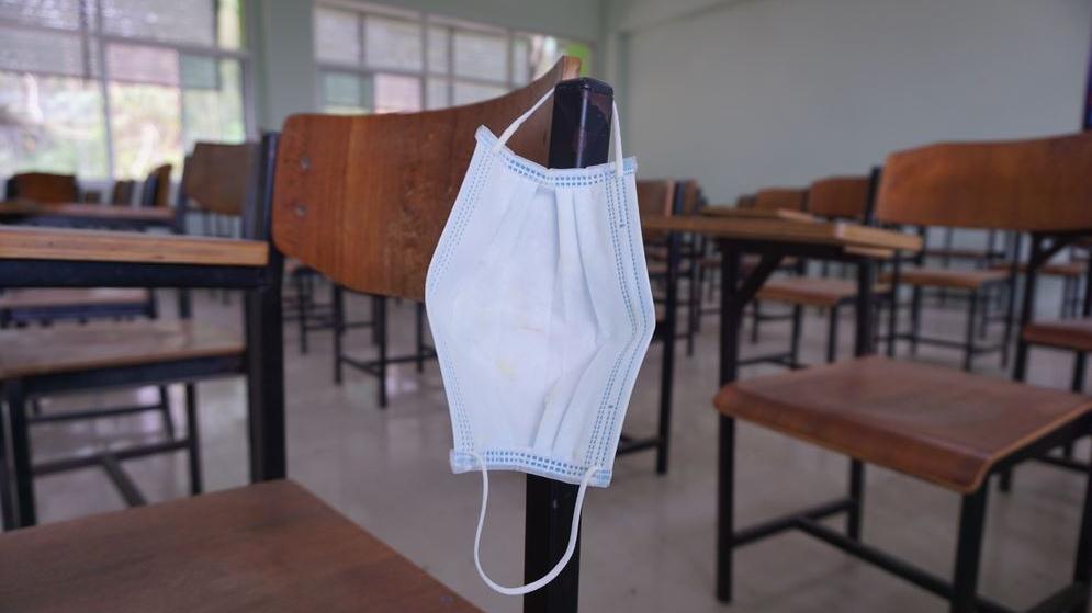 Sala de aula vazia com máscara pendurada em cadeira