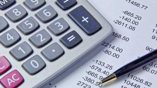 Foto ilustrativa com calculadora, extrato bancário e caneta sobre a mesa