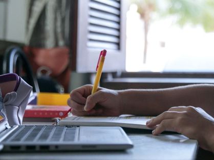 computador e mão segurando caneta sobre caderno