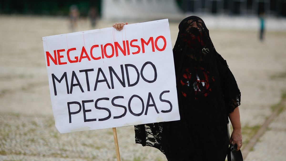 Mulher vestida de preto segurando cartaz contra negacionismo